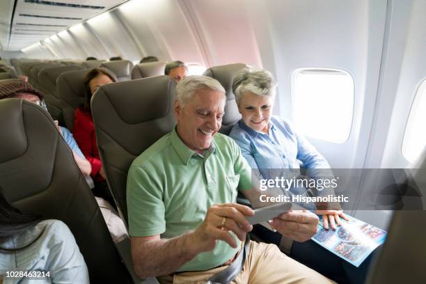 senior pareja viajando por avión y utilizando su teléfono móvil a bordo - aircraft wifi fotografías e imágenes de stock