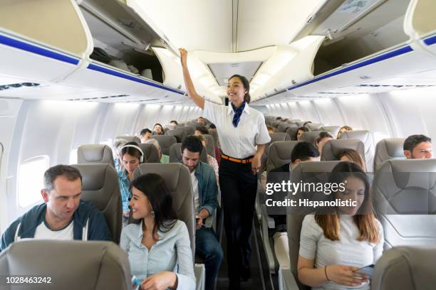 happy flight attendant walking the aisle in an airplane closing overhead compartments - passenger stock pictures, royalty-free photos & images