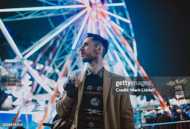 stylish young man at a carnival/funfair standing in front of a big wheel - mark ferris stock pictures, royalty-free photos & images