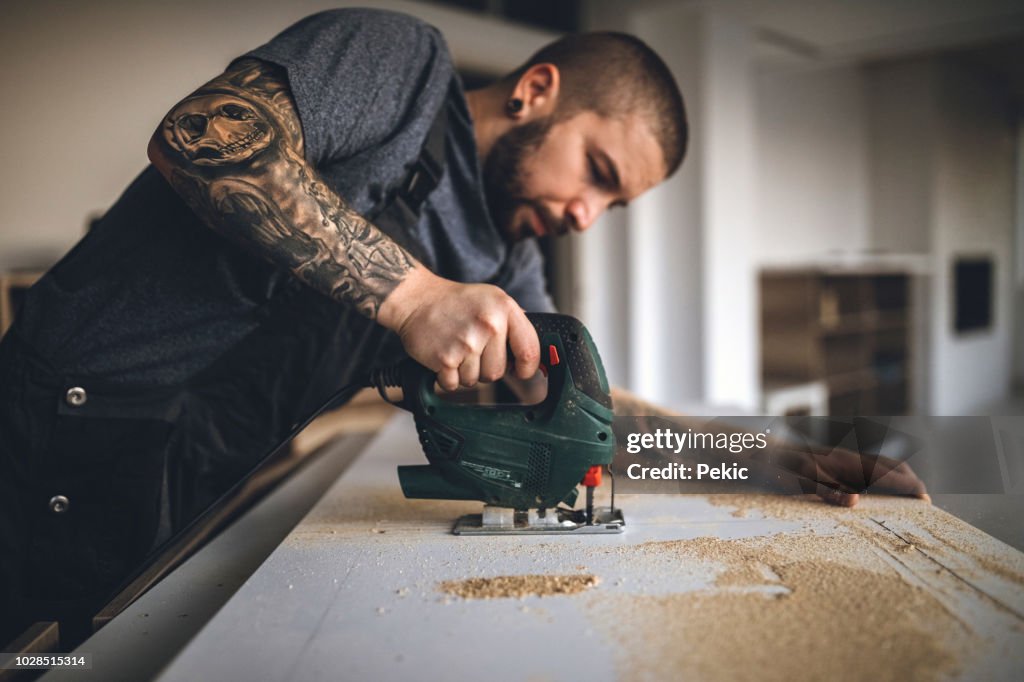 Tätowierte Handy Man Brett Bohren und befestigen neuen Holztisch