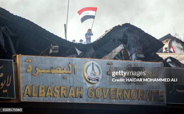 An Iraqi protester waves a national flag while demonstrating outside the burnt-down local government headquarters in the southern city of Basra on...