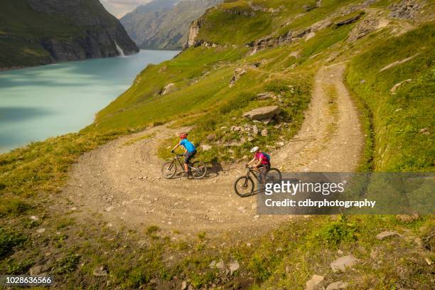 pareja ciclismo de montaña en paisajes alpinos, suiza. - verbier fotografías e imágenes de stock