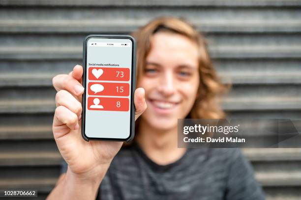 smiling young man showing off his social media notifications on his mobile phone. - man showing phone stock pictures, royalty-free photos & images