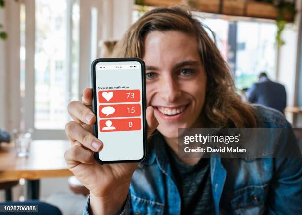 young man in cafe, showing off his social media notifications on his mobile phone. - showing mobile stock pictures, royalty-free photos & images