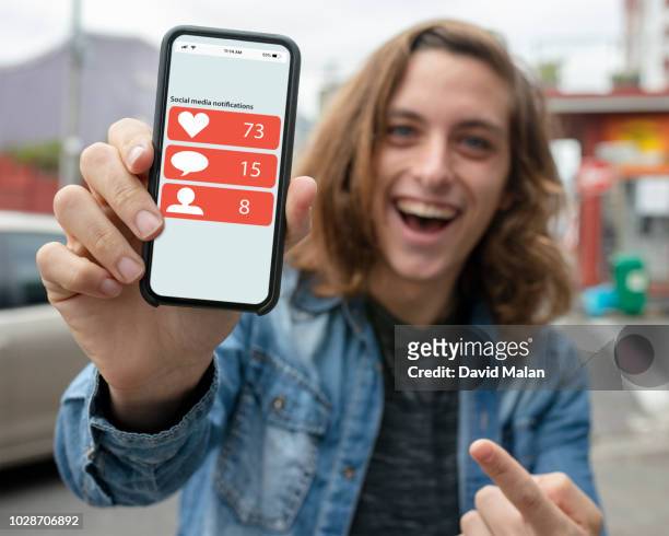 laughing young man in street, showing off his social media notifications on his mobile phone. - mostrare foto e immagini stock