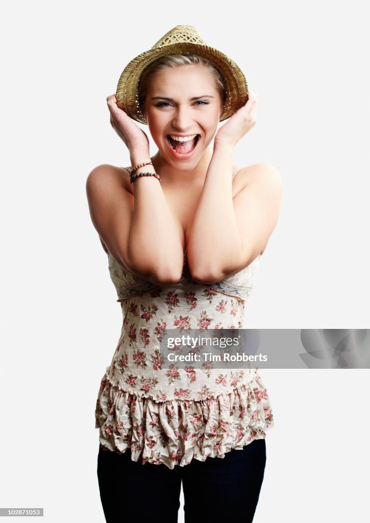 Excited young woman holding hat and shouting.