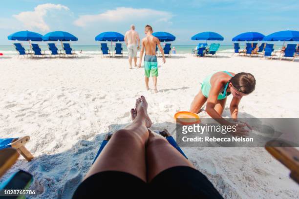 personal persepective of mother in lounge chair watching her son, daughter and husband play on the beach - beach florida family stockfoto's en -beelden