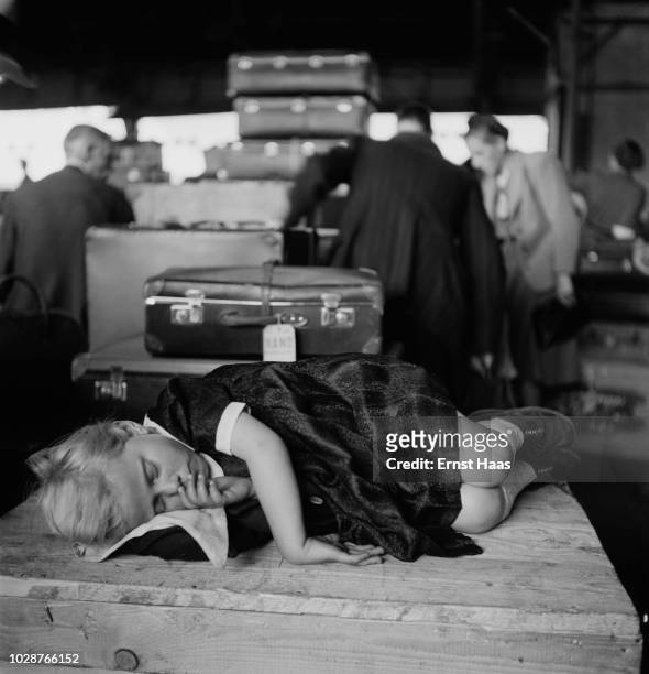 Girl, who has just arrived at Ellis Island in New York, curls up on a packing case to sleep, 1951. She arrived on the USS General R. M. Blatchford,...
