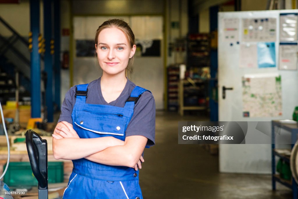 Porträt einer lächelnden jungen Auszubildenden in der Metallindustrie, Arme verschränkt
