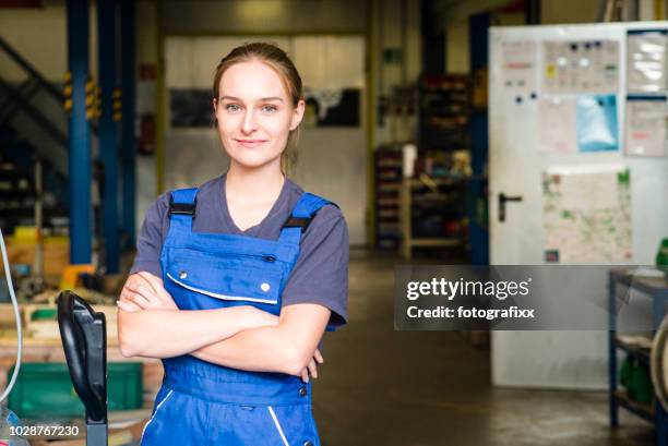 retrato de sonriente mujer joven aprendiz en industria del metal, brazos cruzados - technician fotografías e imágenes de stock