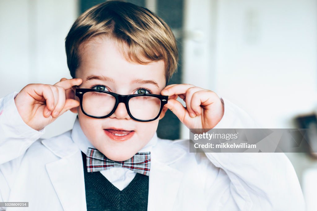 Child wears lab coat and big glasses and looks like a scientist