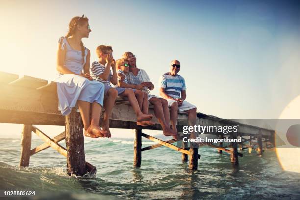 familie sitzt am pier am meer - spanien urlaub stock-fotos und bilder