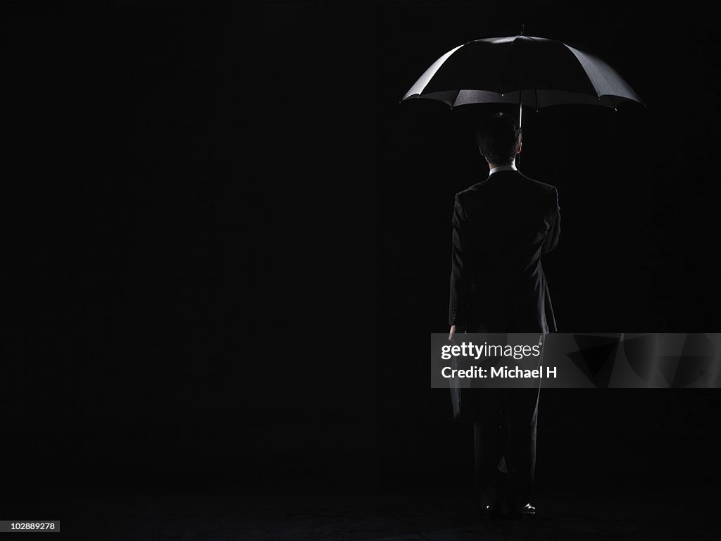 Businessman who is standing under cover of an umbr