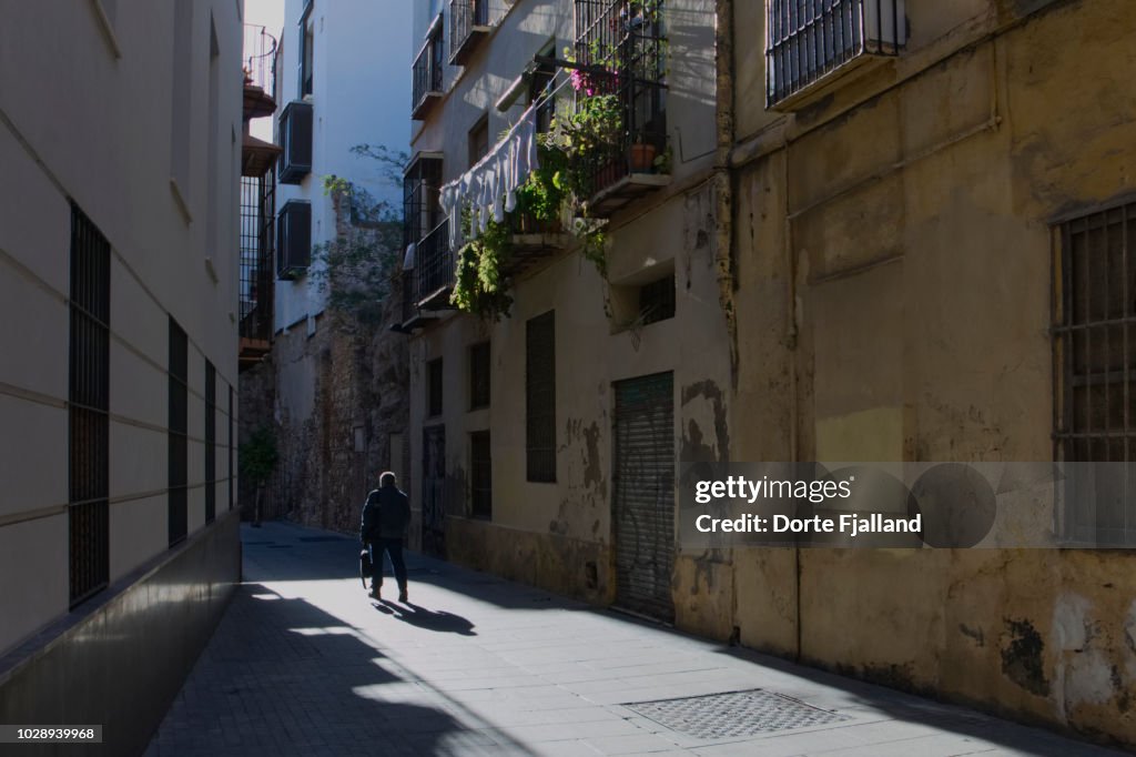 A man walking in the middle of a narrow street with strong sunlight and dark shadows