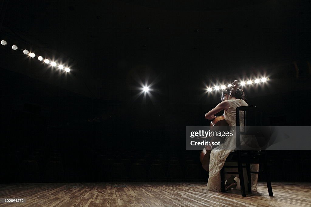 A female cellist playing cello on stage, rear view