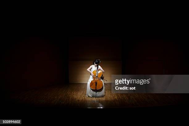 a female cellist playing cello on stage. - spotlight person stock pictures, royalty-free photos & images