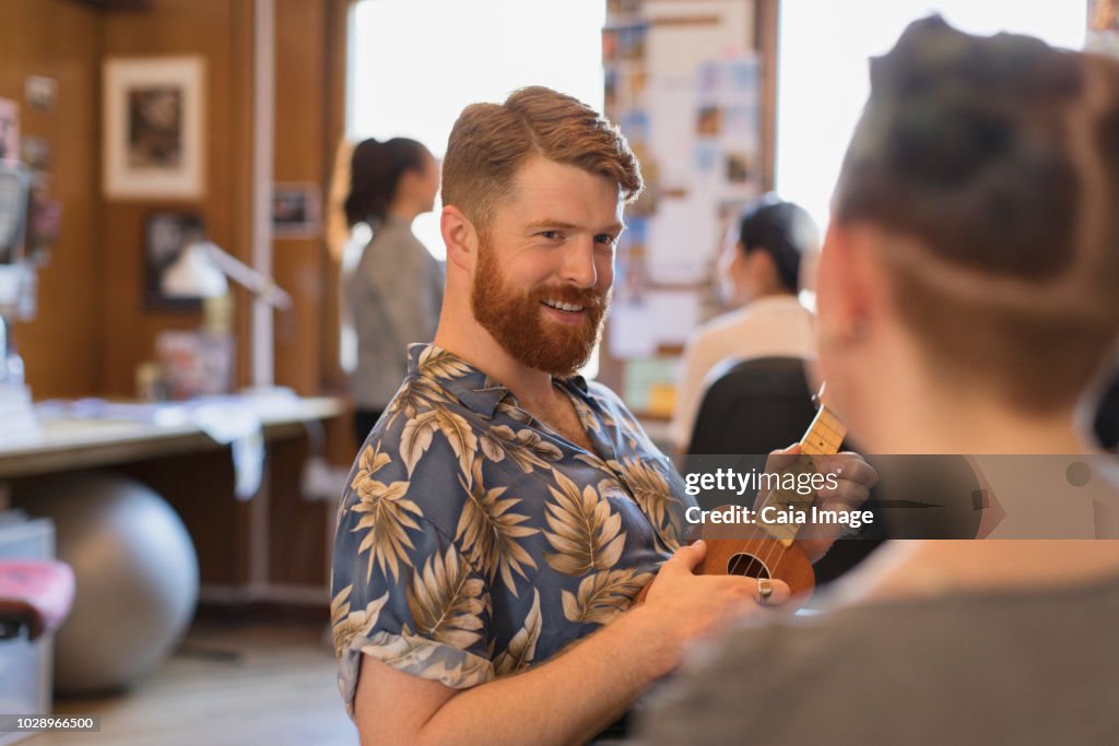 Smiling creative businessman playing ukulele in office