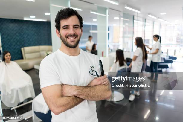 professiona male hair stylist at his business looking at camera smiling with arms crossed while holding scissors and a comb - cabeleireiro imagens e fotografias de stock