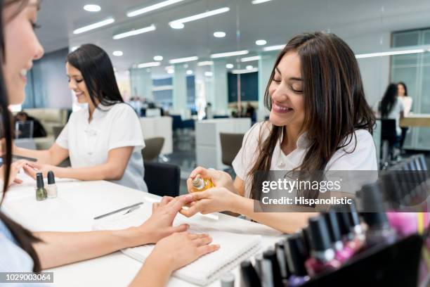 friendly nail technician applying a product on customers hands - fingernail imagens e fotografias de stock