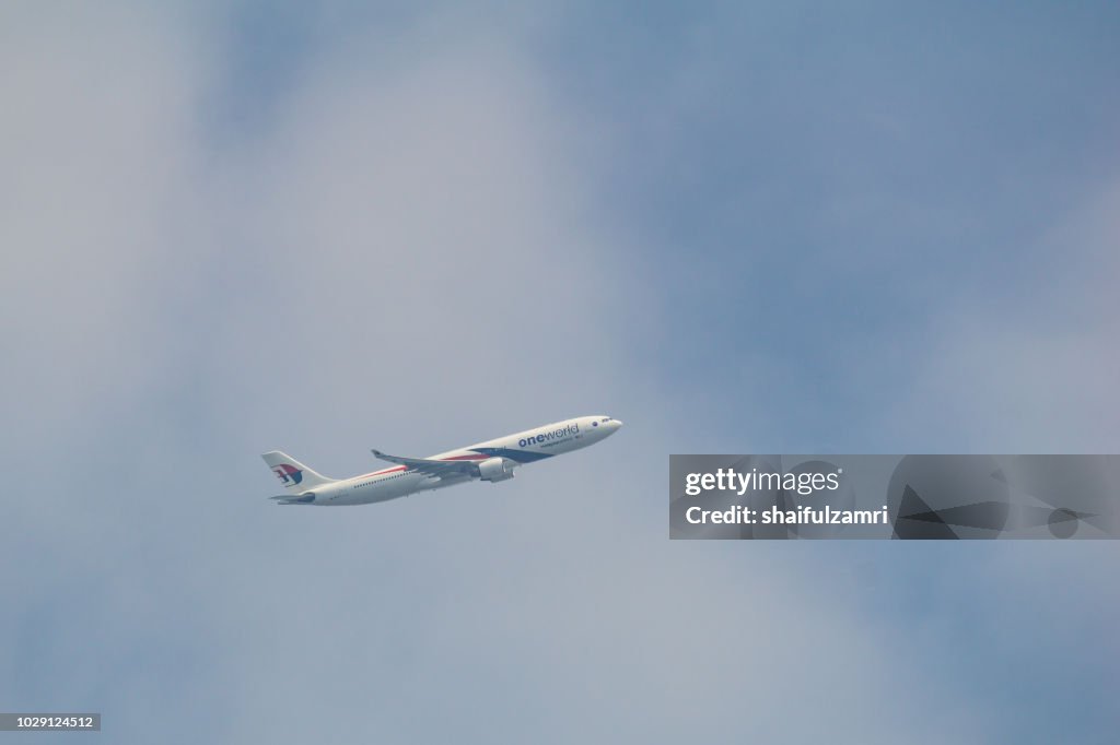 Passenger jet air plane from Malaysia Airlines flying on blue sky over white clouds.