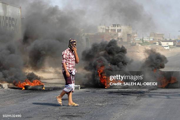 Yemeni man walks by burning tyres as protesters demonstrate against inflation and the rise of living costs in the country's second city of Aden on...