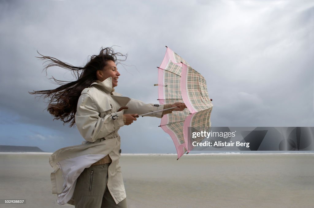 Woman with umbrella on windy beach