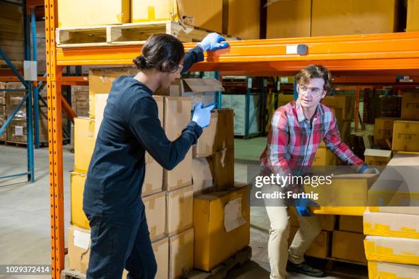 eine männliche lagerarbeiter entfernen einer box unter einige regale, wie ein vorgesetzter ihn auf die richtige technik weist - ergonomie stock-fotos und bilder
