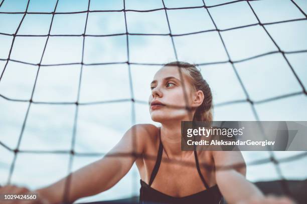 portrait of cute girl leaning on sports net at the beach - girls beach volleyball stock pictures, royalty-free photos & images