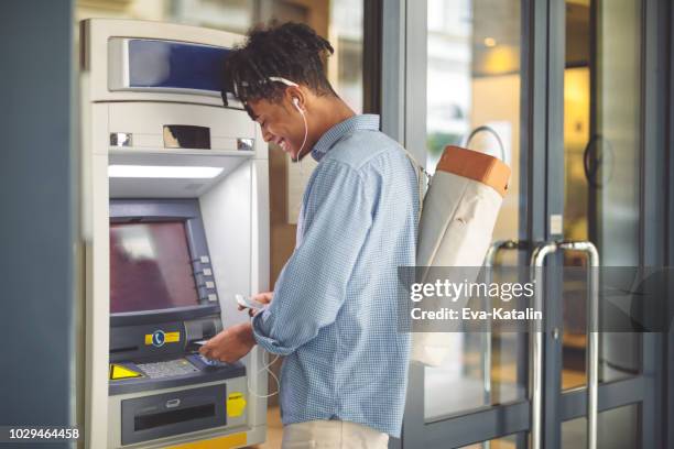 young man is withdrawing money from an atm - atm stock pictures, royalty-free photos & images