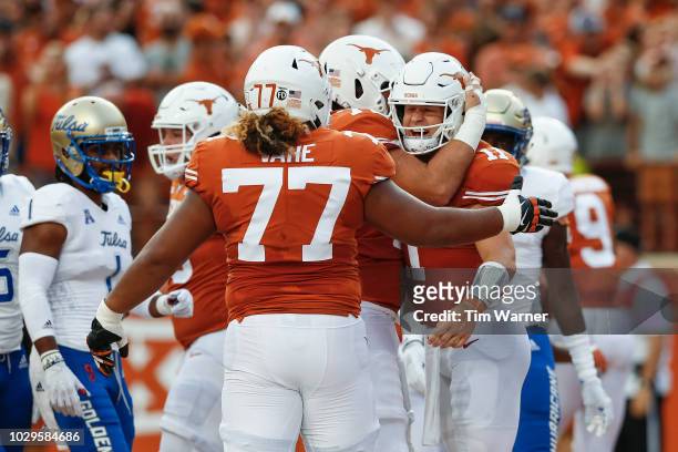 Sam Ehlinger of the Texas Longhorns is congratulated by Patrick Vahe and Elijah Rodriguez after a touchdown in the first quarter against the Tulsa...