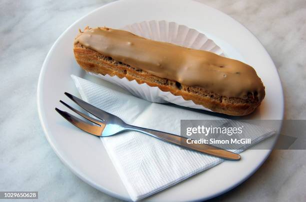 coffee eclair in a paper case served on a white plate with a cake fork and paper napkin - paper napkin stock-fotos und bilder