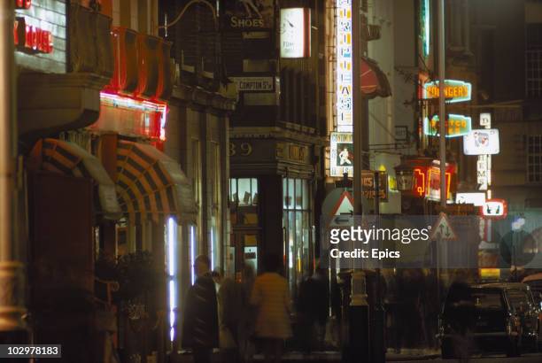 Neon signs illuminate the corner of Old Compton street, Soho, October 1970. Visible are signs for an adult revue and the Golden Lion pub on Dean...