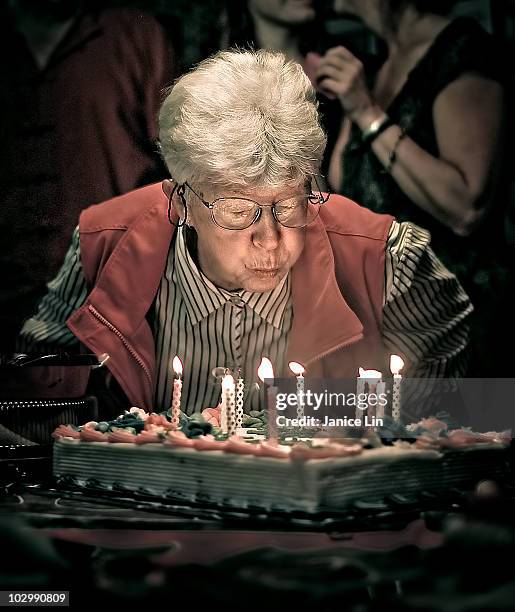 older woman blows out birthday candles - birthday candle fotografías e imágenes de stock