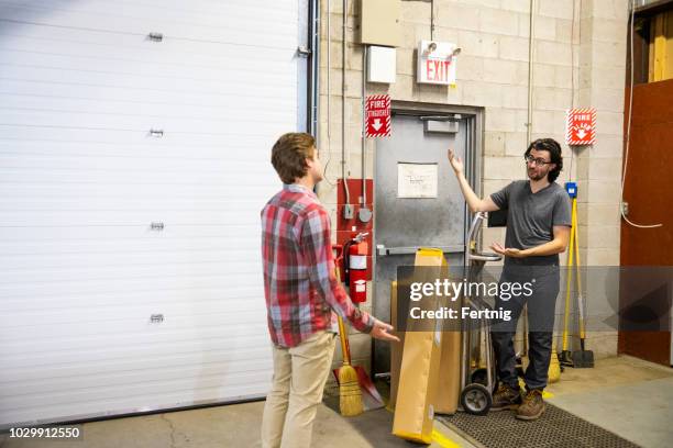 a blocked fire exit door in a warehouse. a supervisor is explaining the dangers of blocking an emergency exit to a new employee. - blocking door stock pictures, royalty-free photos & images