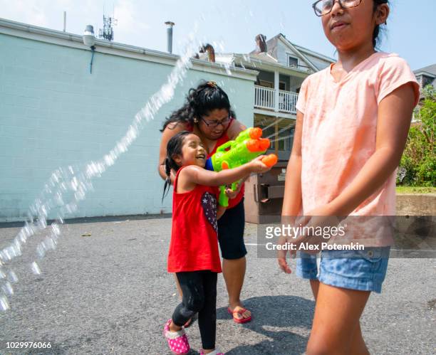 the big happy latino, mexican-american family - the mother, body-positive optimistic smiley woman, and kids, girls of different ages - playing outdoor with a water gun and having fun - hot mexican girls stock pictures, royalty-free photos & images