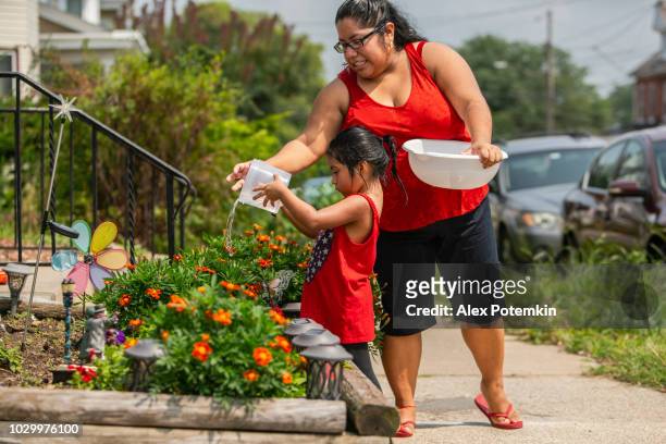die großen glücklich latino, mexikanisch-amerikanischen familie. das kleine mädchen bewässerung blumen in der nähe der veranda, als ihre mutter und schwestern beobachten - hot mexican girls stock-fotos und bilder
