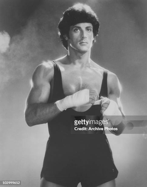 American actor Sylvester Stallone in a vest and shorts, placing boxing tape on his hands circa 1970's.