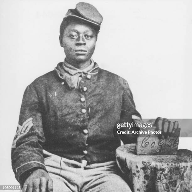 An African American Union soldier of the American Civil War, seated, in a studio portrait, USA, circa 1863. The soldier holds a book in his left...