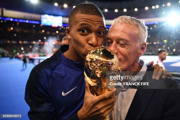 France's midfielder Kylian Mbappe and France's coach Didier Deschamps kiss the 2018 World Cup trophy as they celebrate during a ceremony for the...