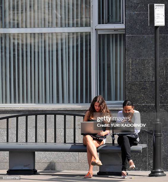 Russian teenage girls work on laptop computers while wating for a public bus in Moscow on August 11, 2009. A survey by Russia's Levada Center found...