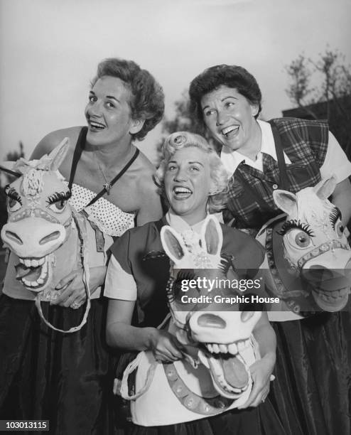 The Andrews Sisters smiling and with toy horses heads, USA, circa 1950.