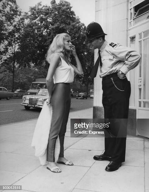 Actress Ursula Andress talking to a policeman in London, England, 6th August 1964. Andress was in Britain to shoot 'She' at Elstree Studios.