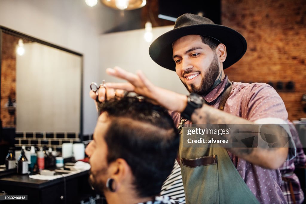 Smiling barber cutting customer's hair in salon