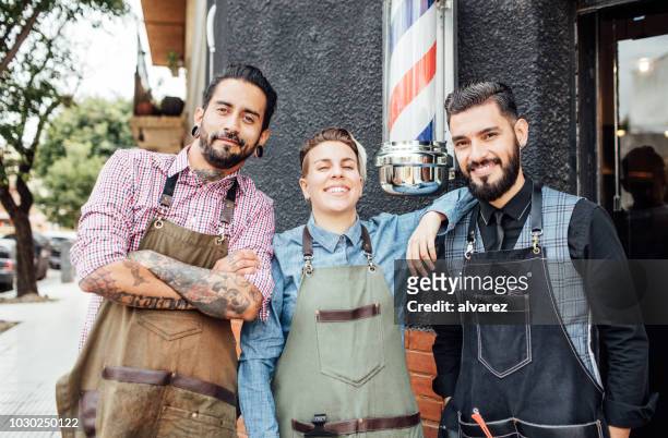 smiling barbers standing outside hair salon - 3 men standing outside stock pictures, royalty-free photos & images