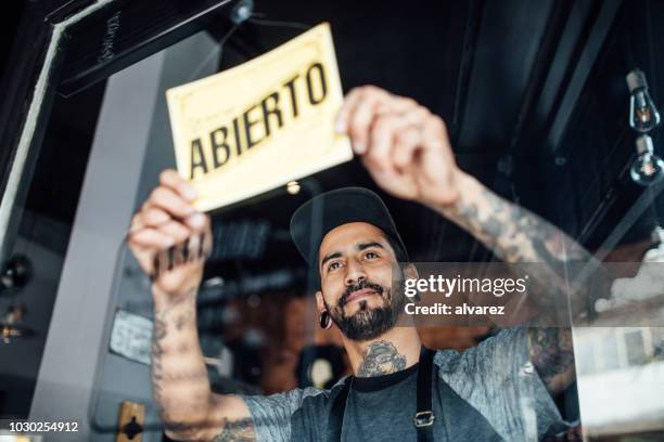 peluquero masculino colgando una muestra abierta en la puerta de cristal - acto de apertura fotografías e imágenes de stock