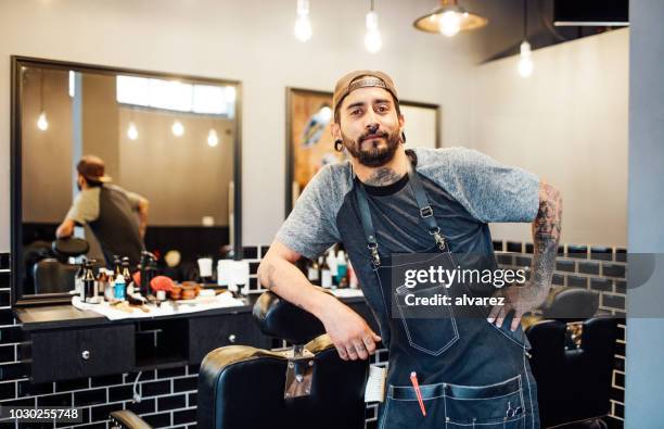 portret van kapper leunend op stoel in salon - barbers stockfoto's en -beelden