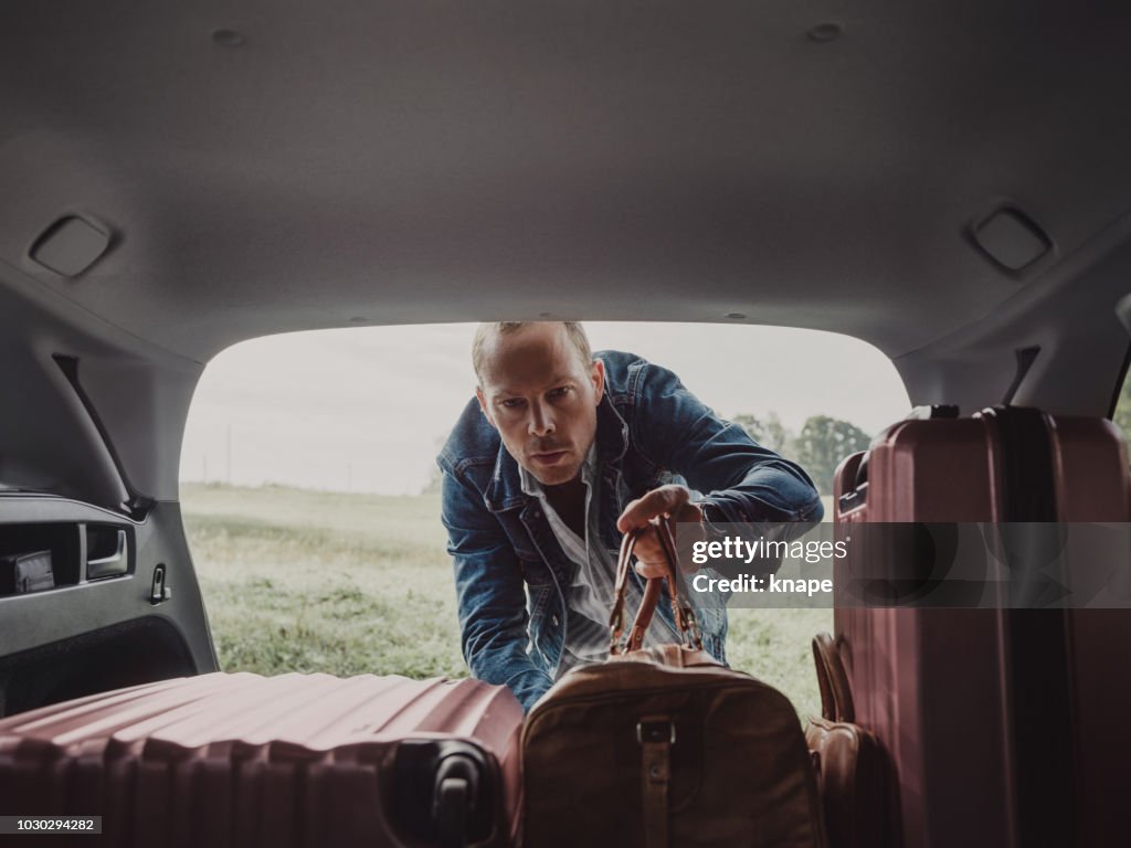 Man packing in his luggage suitcase in his car ready for road trip