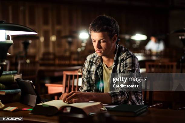 young man reading in library at night - history textbook stock pictures, royalty-free photos & images