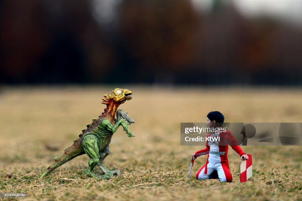 Holding the shield and the sword of the boy kneeling on the ground, with the dinosaur on the visual