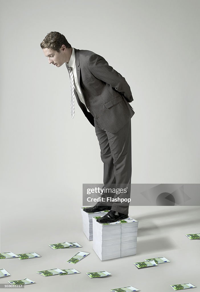 Businessman standing on large pile of Euro notes